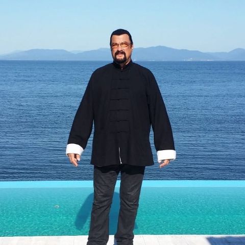 Steven Seagal is in front of the sea.
